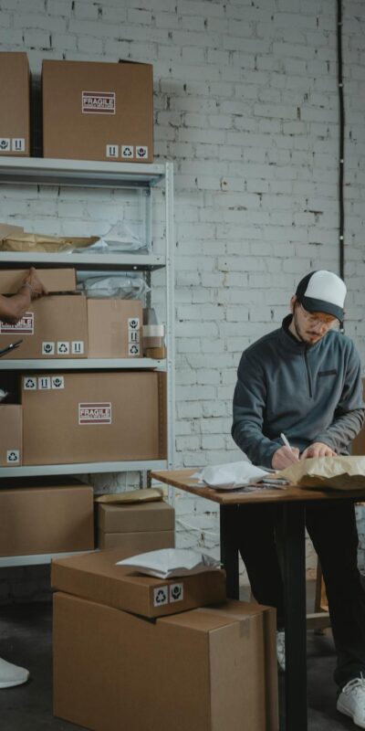 Two workers handling packages and organizing stock in a warehouse setting.